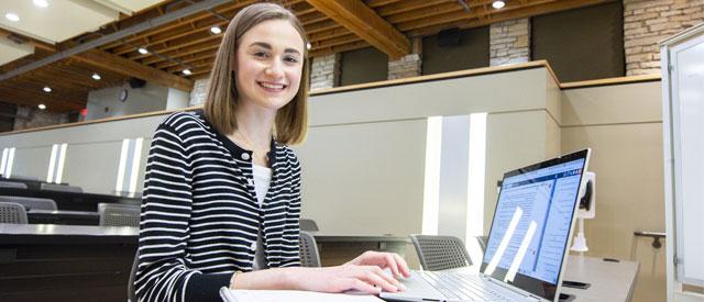 一名博天堂官方入口登陆登录的学生对着镜头微笑，在笔记本电脑上工作.